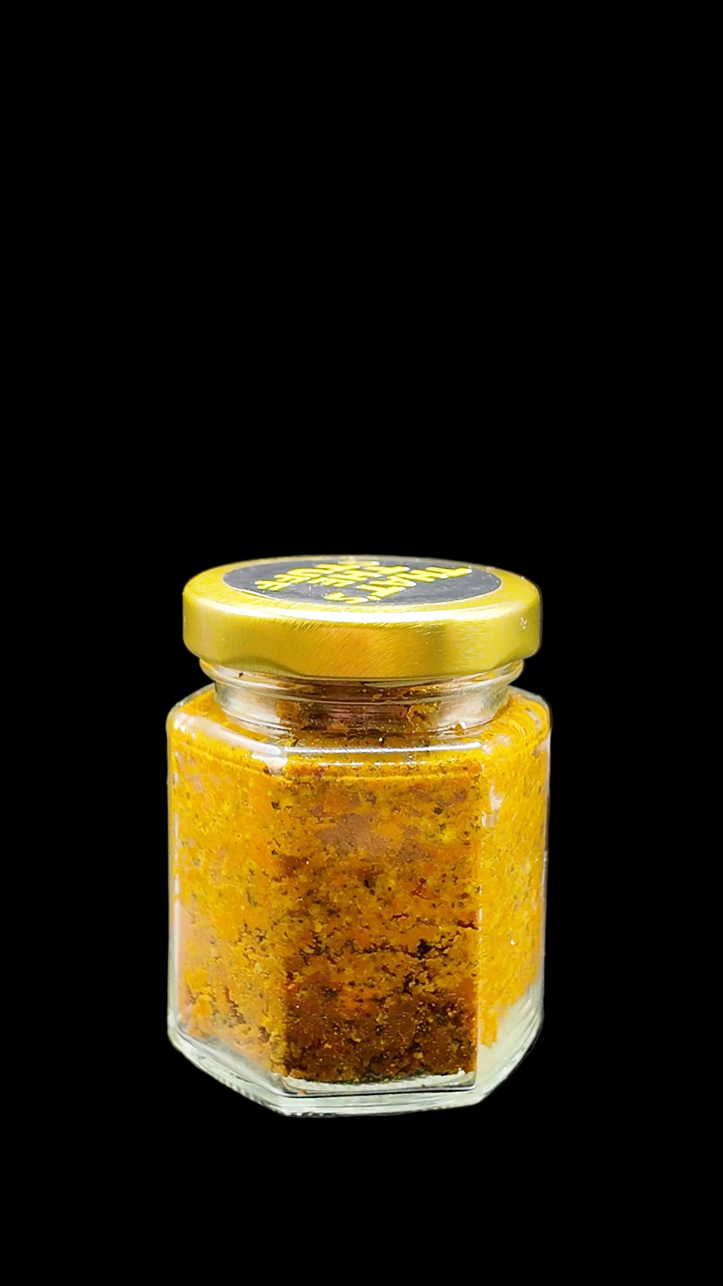 Small glass jar of turmeric with peppercorn a gold lid on a black background