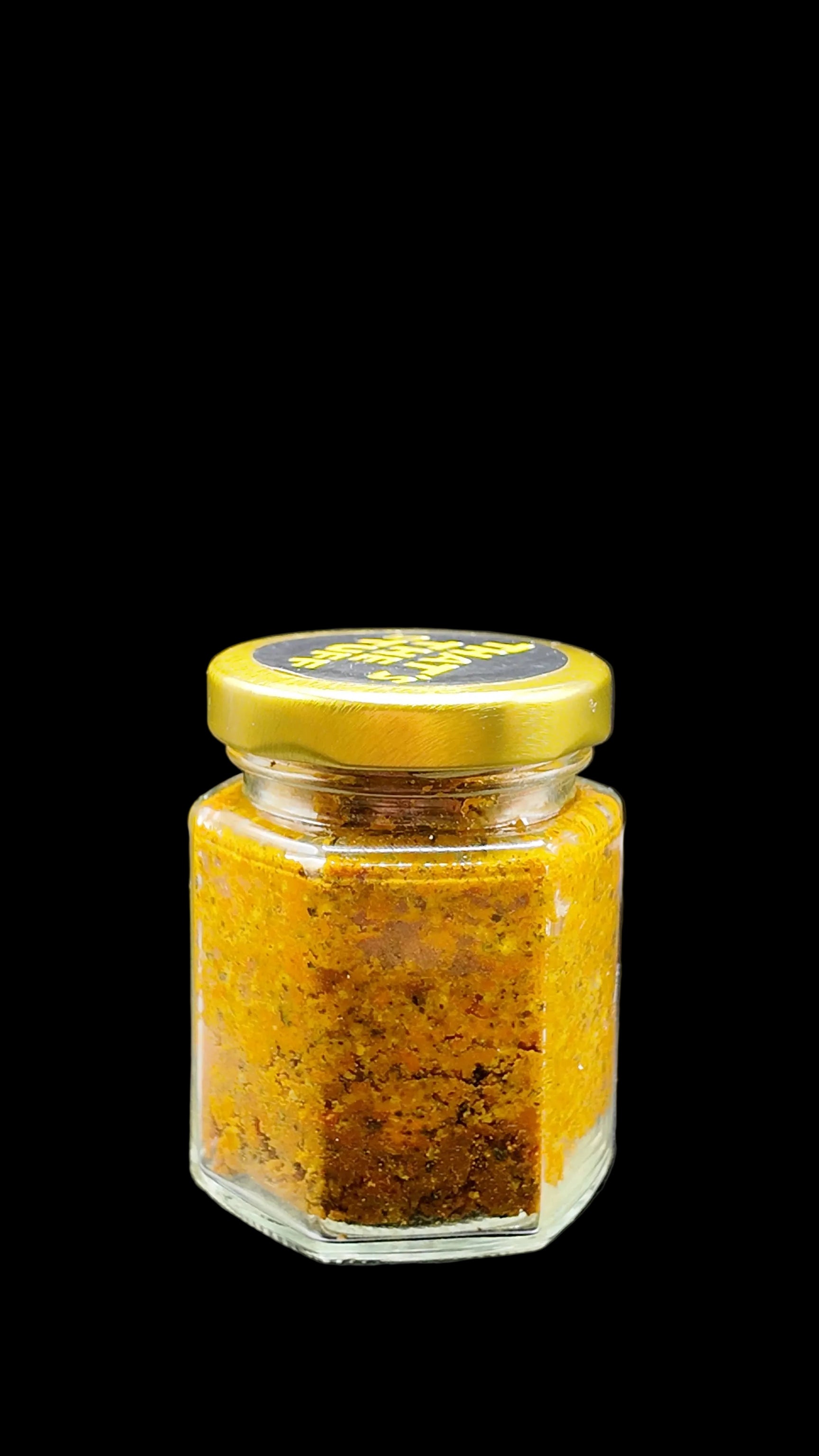 Small glass jar of turmeric with peppercorn a gold lid on a black background